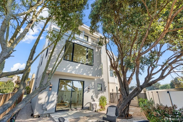 rear view of property with stucco siding, fence, a balcony, and a patio