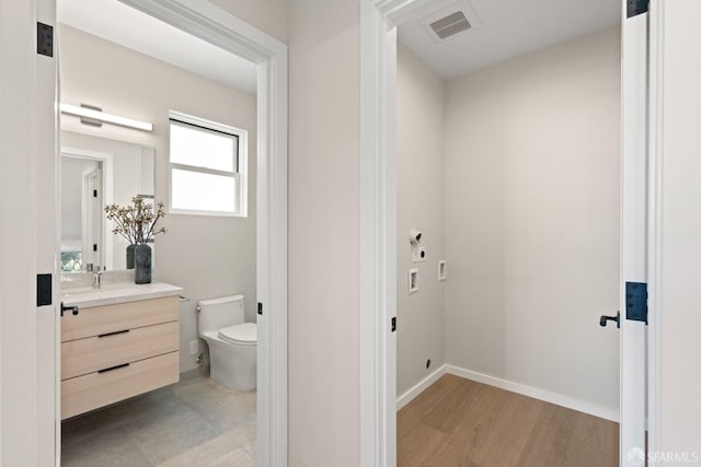 half bath with toilet, vanity, baseboards, and wood finished floors