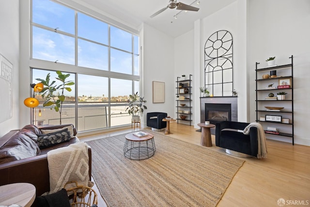 living room featuring a glass covered fireplace, ceiling fan, a towering ceiling, and wood finished floors