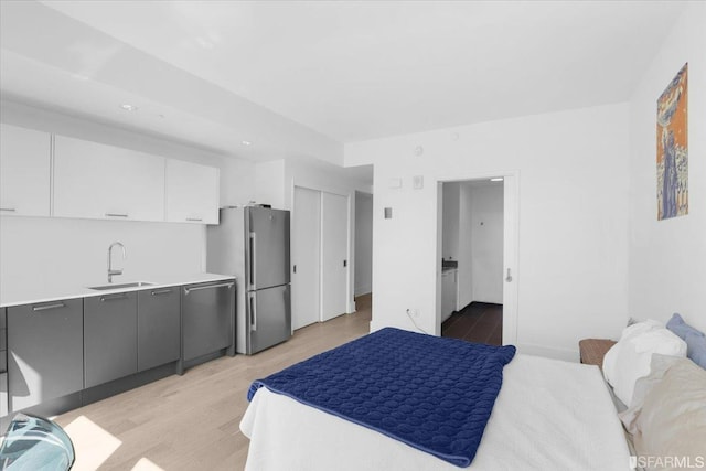 bedroom featuring stainless steel refrigerator, sink, and light wood-type flooring