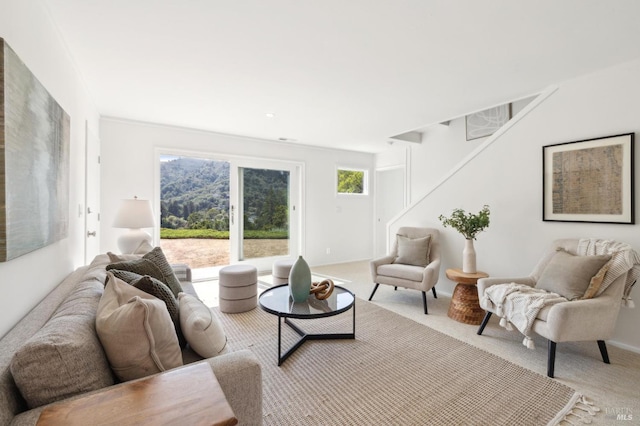 living area featuring a wealth of natural light, stairs, and light colored carpet