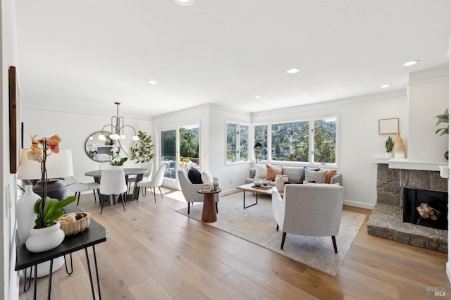 living room with a fireplace, light wood-style flooring, recessed lighting, a notable chandelier, and baseboards