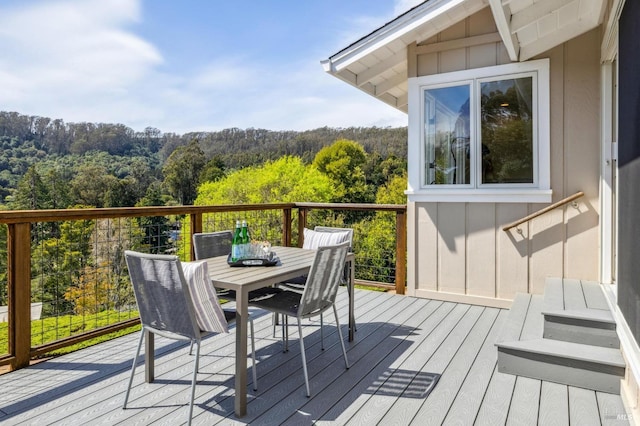 wooden terrace with a view of trees and outdoor dining area