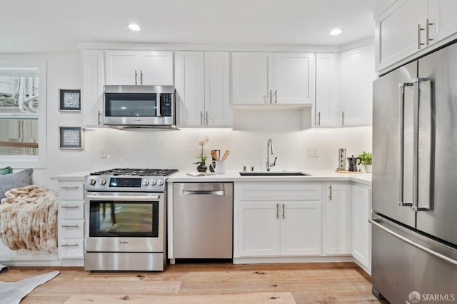 kitchen featuring white cabinetry, sink, light wood-type flooring, and premium appliances