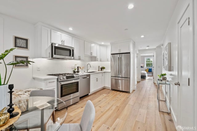 kitchen with sink, high quality appliances, light hardwood / wood-style floors, decorative backsplash, and white cabinets