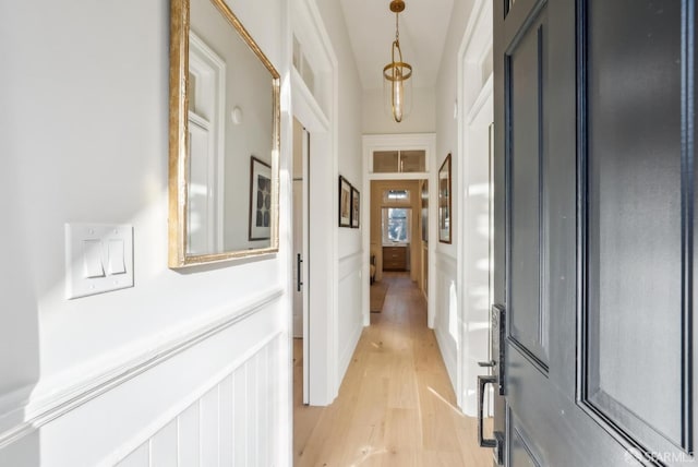 corridor featuring light wood-style floors, wainscoting, and a decorative wall