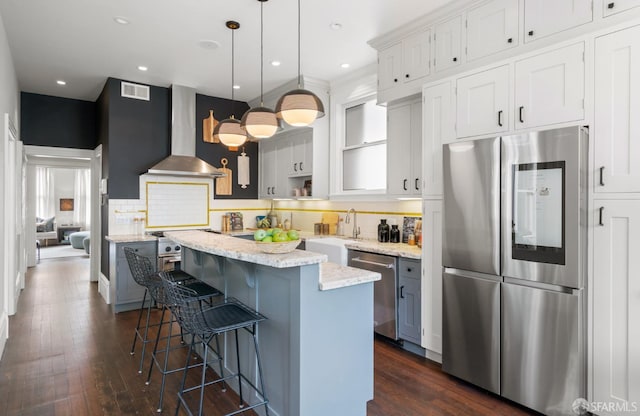 kitchen with wall chimney exhaust hood, dark wood-style floors, a kitchen island, and appliances with stainless steel finishes