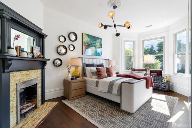 bedroom featuring a tiled fireplace, visible vents, a notable chandelier, and dark wood-style flooring