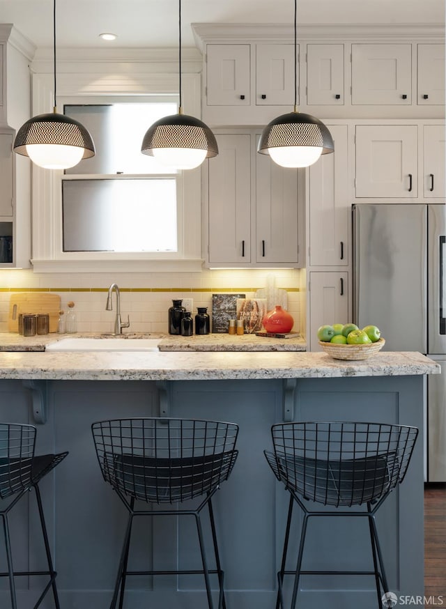 kitchen featuring white cabinets, a sink, freestanding refrigerator, decorative light fixtures, and a breakfast bar area