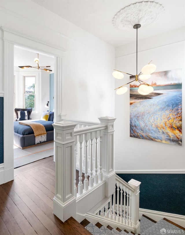 stairway with baseboards, a chandelier, and hardwood / wood-style floors