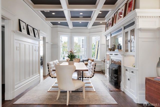 dining space with a fireplace with flush hearth, coffered ceiling, beamed ceiling, a decorative wall, and dark wood-style flooring