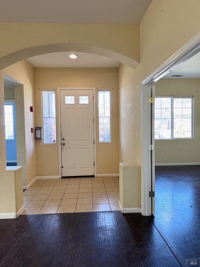 foyer entrance with a wealth of natural light, arched walkways, baseboards, and wood finished floors