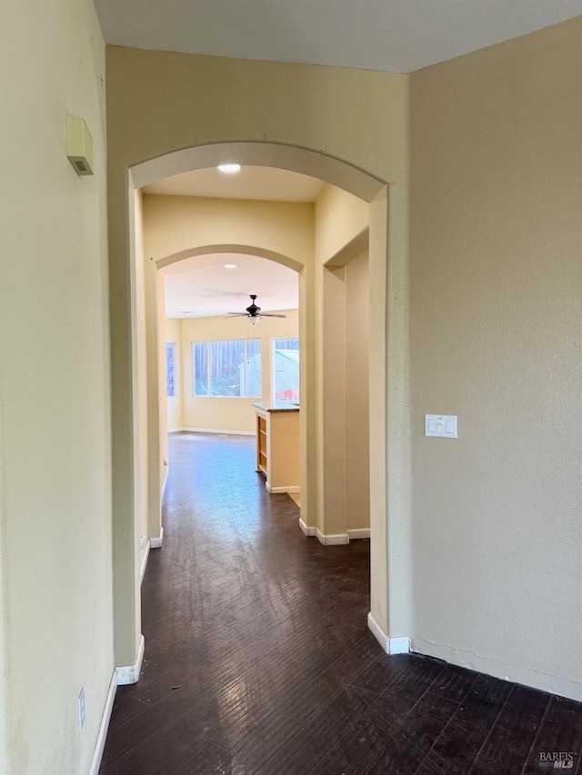 hall featuring arched walkways, dark wood-style floors, and baseboards