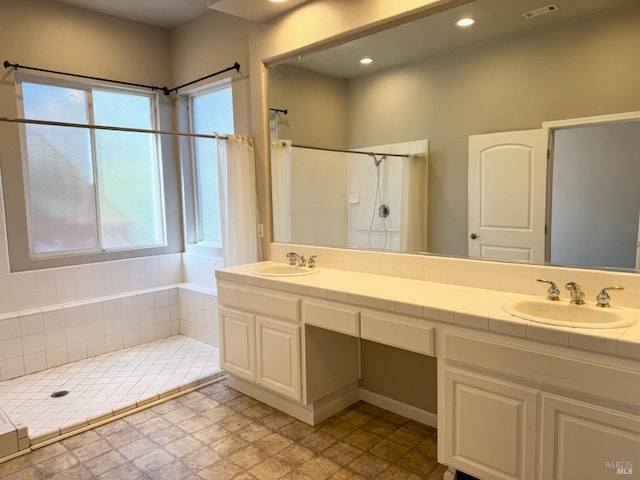 bathroom with a tile shower, double vanity, a sink, and recessed lighting