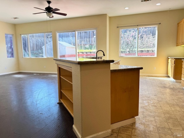 kitchen featuring a healthy amount of sunlight, a center island with sink, baseboards, and ceiling fan