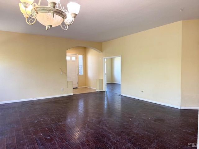 spare room with hardwood / wood-style flooring, baseboards, arched walkways, and a notable chandelier