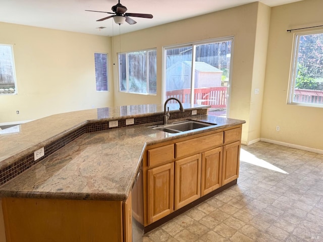 kitchen featuring ceiling fan, stone counters, a sink, baseboards, and light floors