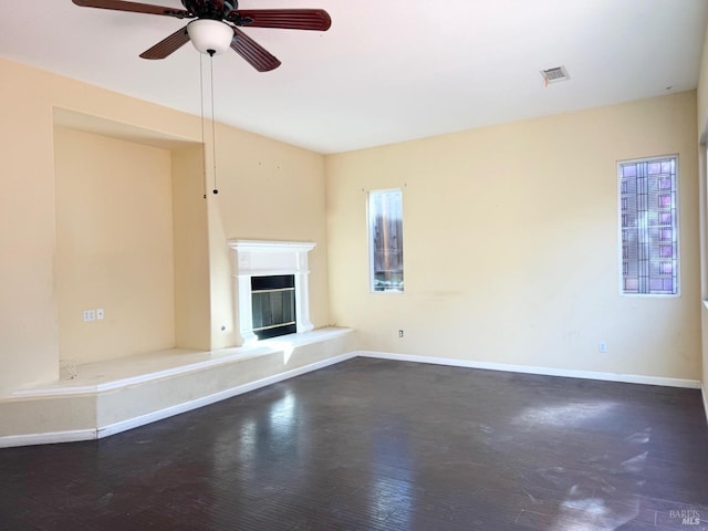 unfurnished living room featuring a wealth of natural light, dark wood-type flooring, a glass covered fireplace, and visible vents