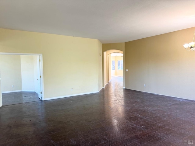 spare room featuring arched walkways, baseboards, dark wood finished floors, and a notable chandelier