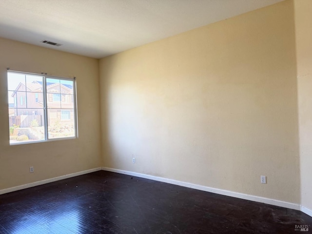 empty room with dark wood-type flooring, visible vents, and baseboards