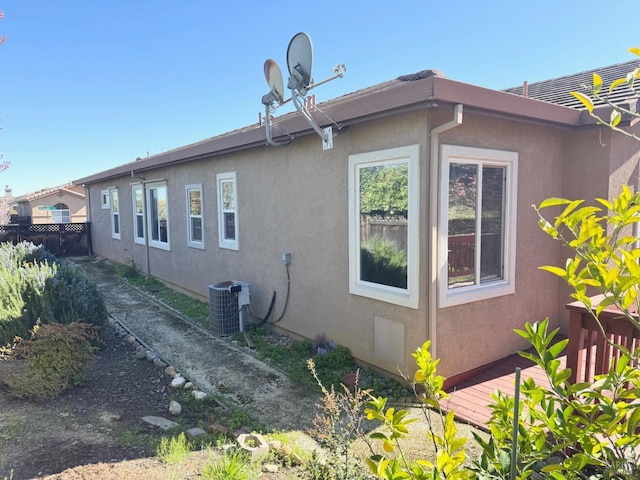 view of side of property featuring central AC, fence, and stucco siding