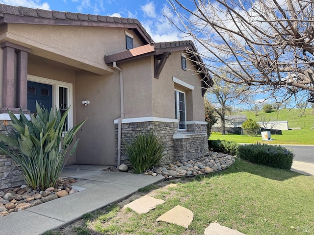 view of property exterior featuring stone siding, a yard, and stucco siding