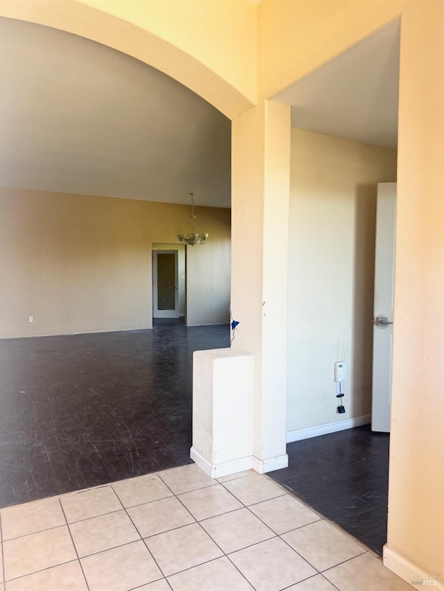 spare room featuring an inviting chandelier, tile patterned flooring, arched walkways, and baseboards