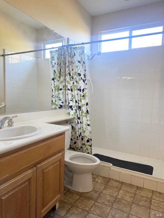 full bathroom featuring a textured wall, a tile shower, vanity, and toilet