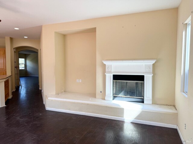 unfurnished living room with arched walkways, recessed lighting, dark wood-style flooring, baseboards, and a glass covered fireplace