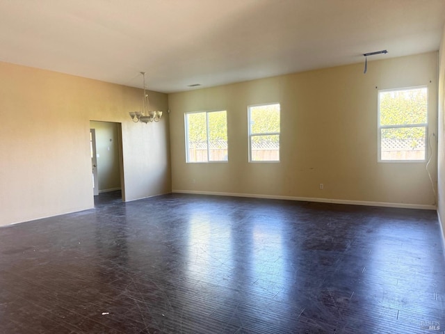 unfurnished room with dark wood-style flooring, a notable chandelier, plenty of natural light, and baseboards