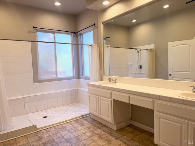 bathroom with recessed lighting, tiled shower, a sink, and double vanity