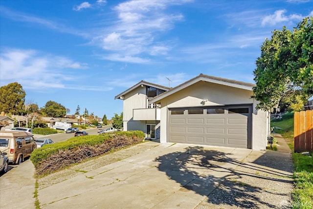 view of front of house featuring a garage, driveway, fence, and stucco siding