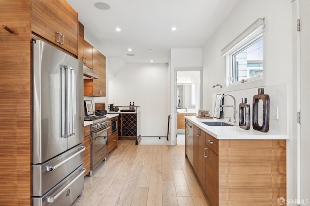 kitchen featuring high end appliances, sink, and light hardwood / wood-style flooring