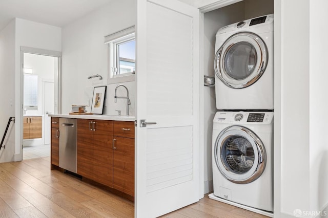 clothes washing area featuring stacked washer and dryer, sink, and light wood-type flooring