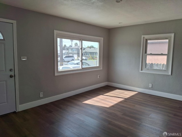 spare room with a textured ceiling, dark wood-type flooring, and baseboards