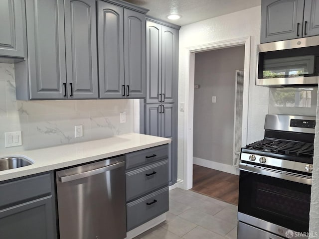 kitchen with decorative backsplash, appliances with stainless steel finishes, light countertops, and gray cabinetry