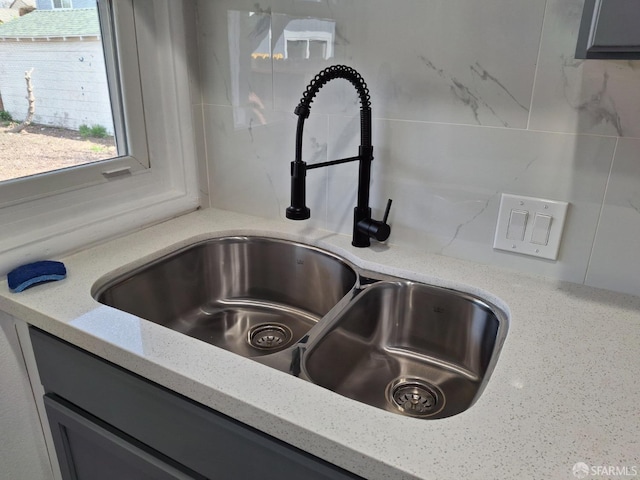 room details with light stone counters, decorative backsplash, gray cabinetry, and a sink