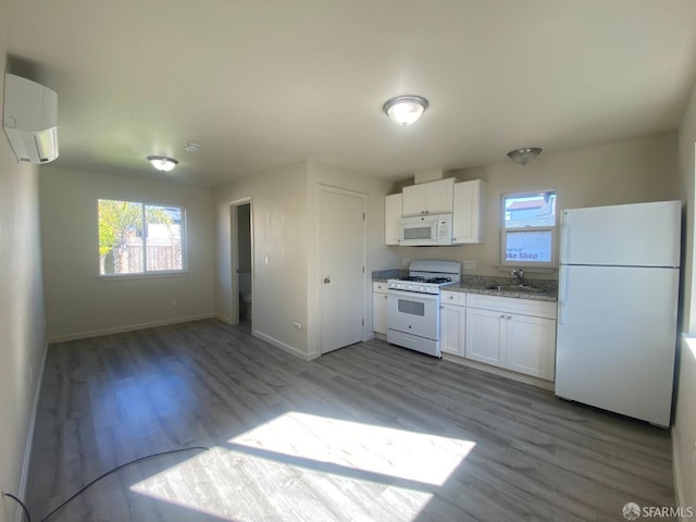 kitchen with white appliances, a sink, an AC wall unit, white cabinets, and a wealth of natural light