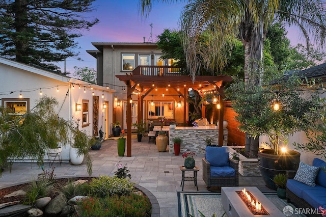 rear view of property featuring an outdoor living space with a fire pit, a patio area, stucco siding, and a balcony