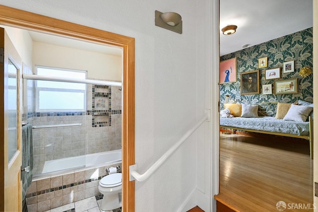 full bath with tiled shower / bath combo, toilet, wallpapered walls, and wainscoting