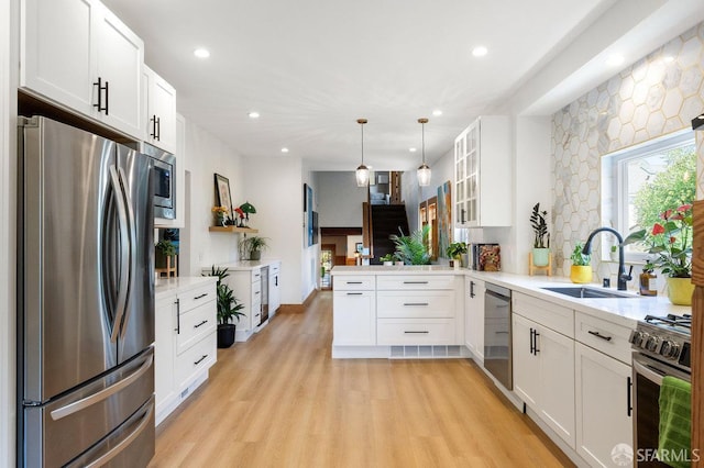 kitchen featuring white cabinets, a sink, stainless steel appliances, a peninsula, and glass insert cabinets