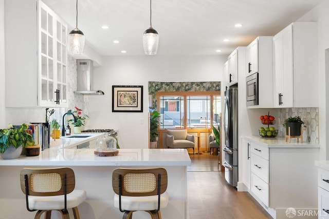 kitchen with wall chimney range hood, a kitchen breakfast bar, stainless steel appliances, and a sink