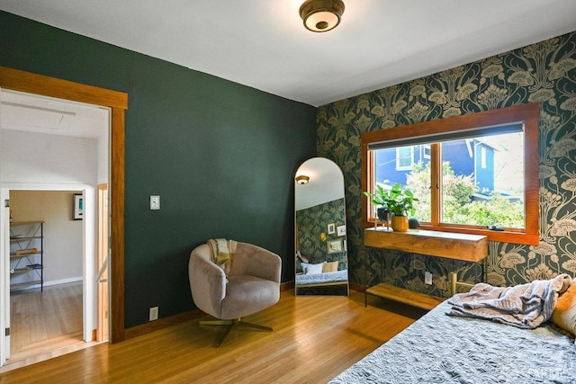 bedroom featuring baseboards, wallpapered walls, and wood finished floors