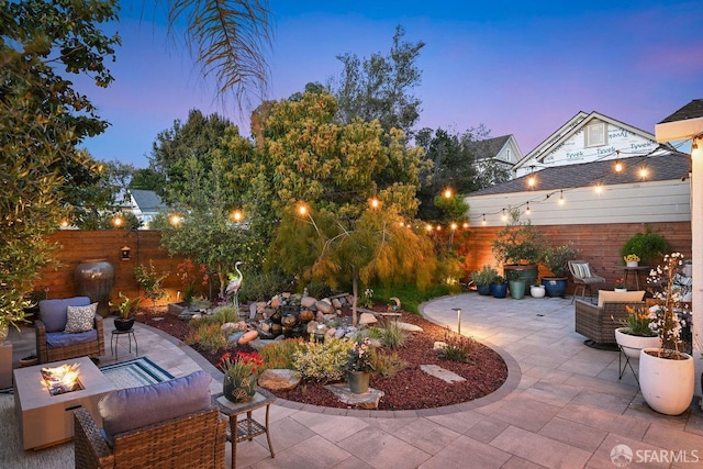 patio terrace at dusk featuring a fenced backyard and an outdoor living space with a fire pit