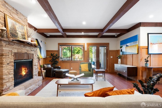 living room with a stone fireplace, beam ceiling, hardwood / wood-style flooring, and a wainscoted wall