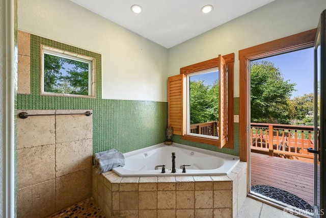 bathroom with a healthy amount of sunlight, tile walls, a jetted tub, and recessed lighting