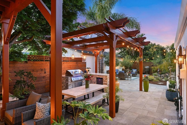 patio terrace at dusk with a pergola, outdoor dining space, a fenced backyard, and an outdoor kitchen