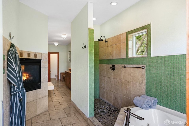 full bath with a jetted tub, stone tile floors, a walk in shower, and a tiled fireplace