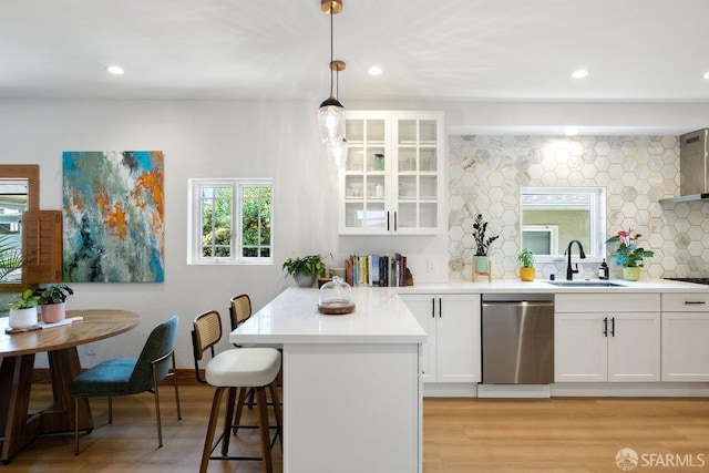 kitchen featuring stainless steel dishwasher, a breakfast bar, white cabinets, a sink, and light wood-style flooring
