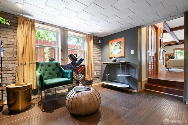 living area featuring baseboards, wood finished floors, and brick wall